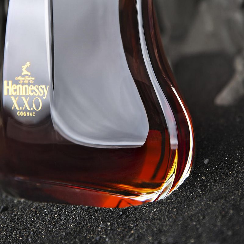 A close-up of a bottle of Hennessy XXO cognac on fine gravel.