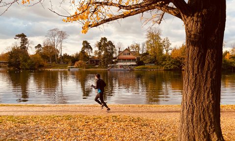 A man running on fall foliage near a lake.