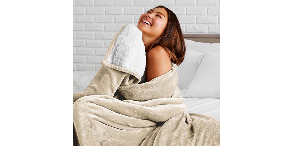A woman holding a Bare Home Sherpa Blanket and smiling.