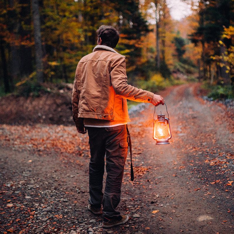 A man with a lantern at a crossroads in the woods.