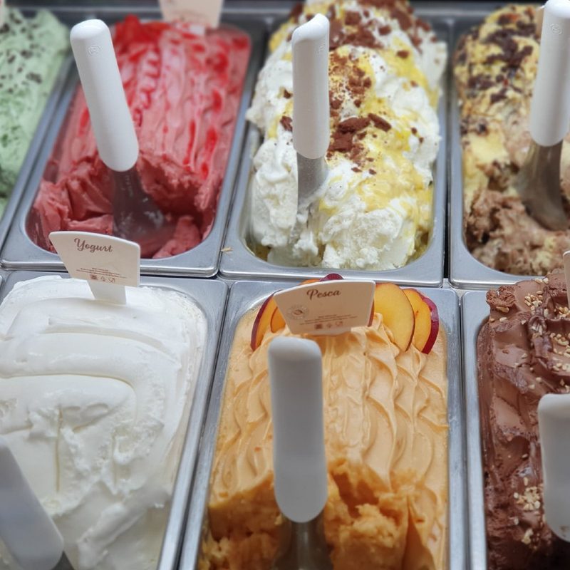 pans of different flavored ice cream with scoops in each one.