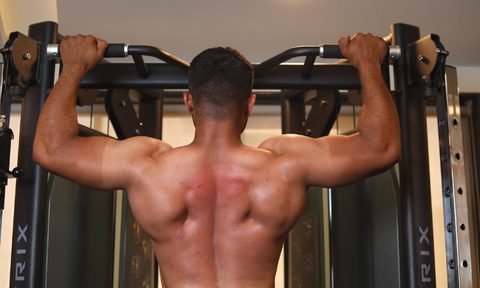 Shirtless man doing a shoulder workout on a pull-up bar