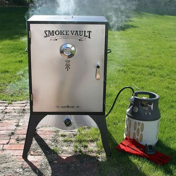 Camp chef smoke vault in a backyard with propane tank attached and smoke coming out of the top.