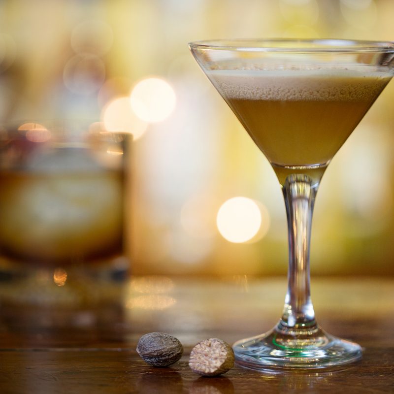 A glass of Brandy Alexander with a cup of cocktail behind it on a table.