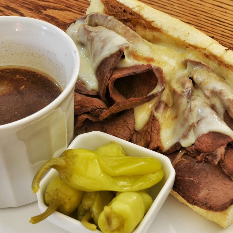 french dip with au jus and peppers on a plate.