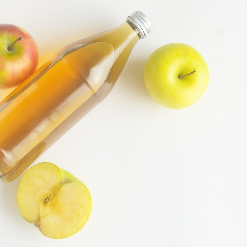 three apples and one bottle of hard cider on a table.