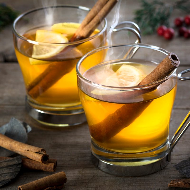 Two glasses of hot toddies with cinnamon sticks on a wooden table.