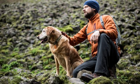 A crouching male hiker and his dog on mossy rocks.