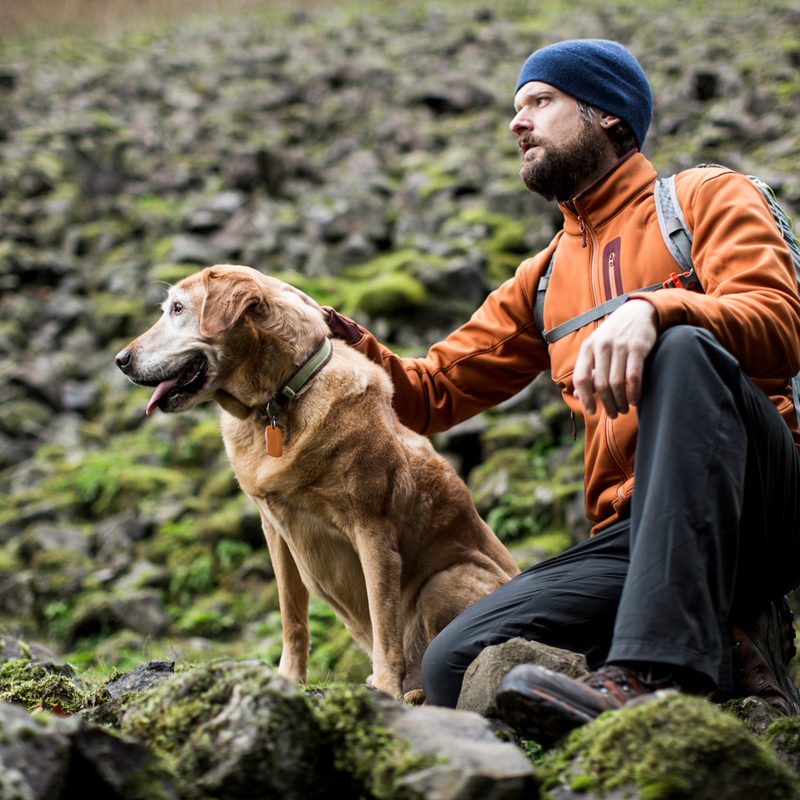 A crouching male hiker and his dog on mossy rocks.