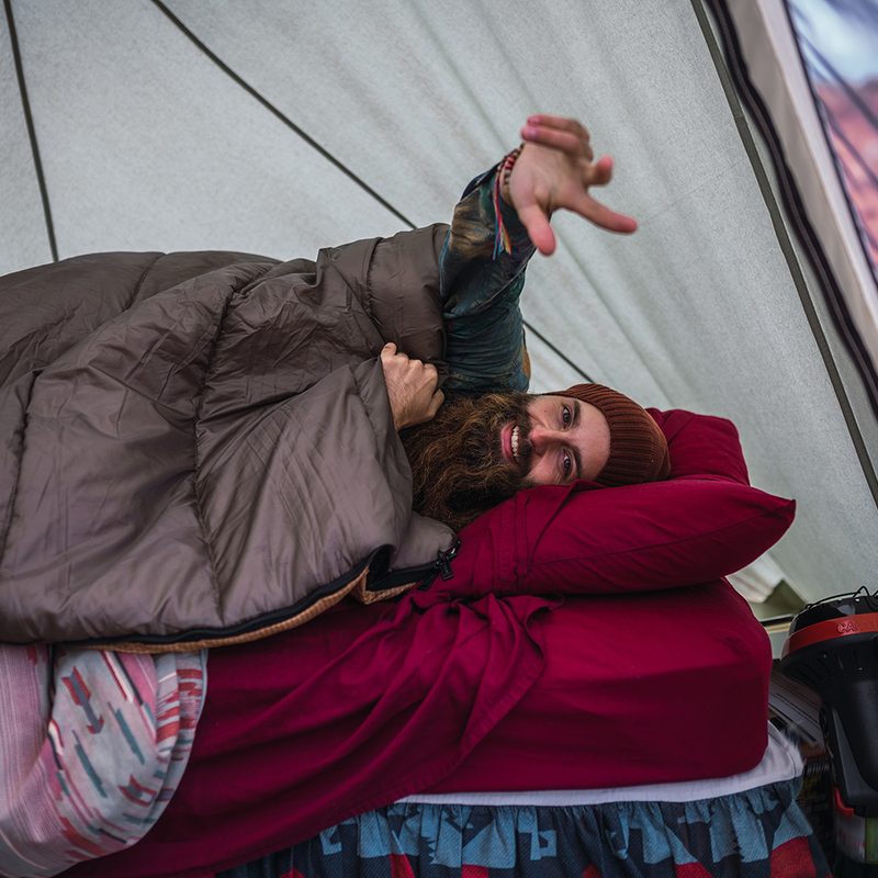 Cheerful traveler lying on bed in tent.