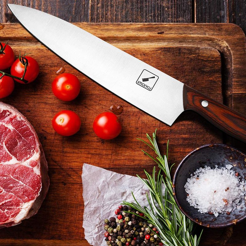 An Imarku knife beside tomatoes, a slab of meat, and other healthy foods on a wooden cutting board.