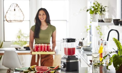KitchenAid K150 3 Speed Ice Crushing Blender being used by a woman to make smoothies in a home kitchen.