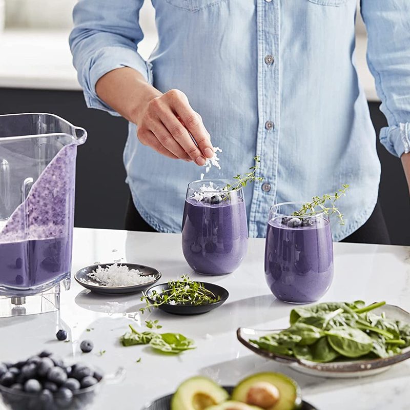 Person making blue smoothies using fresh ingredients using the KitchenAid KSB4027 blender in a kitchen.
