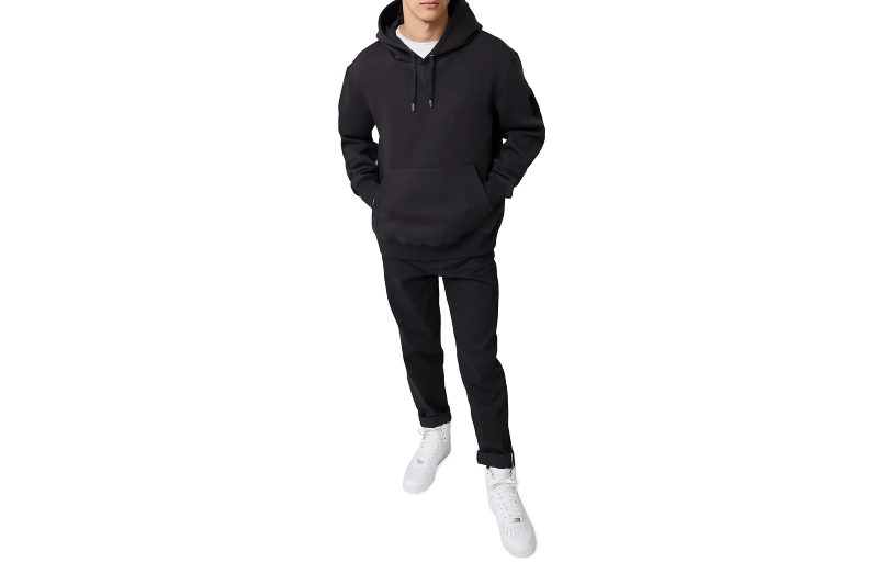 A male model wearing a black Mackage Krys Logo Hoodie, black pants, and white sneakers.