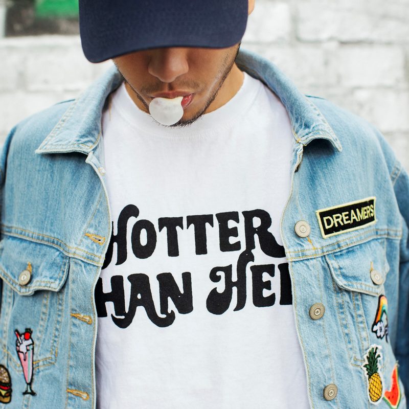 Man wearing a denim jacket over a statement shirt.