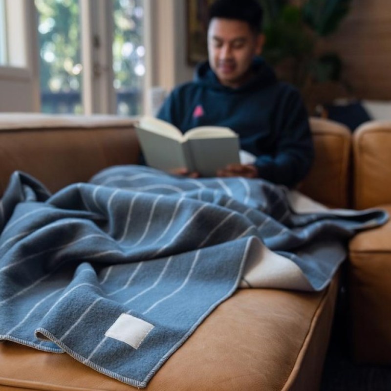 man reading in the background covered by a merino softwool throw blanket.