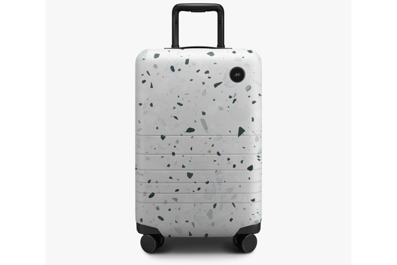 monos carry on luggage against a gray background.