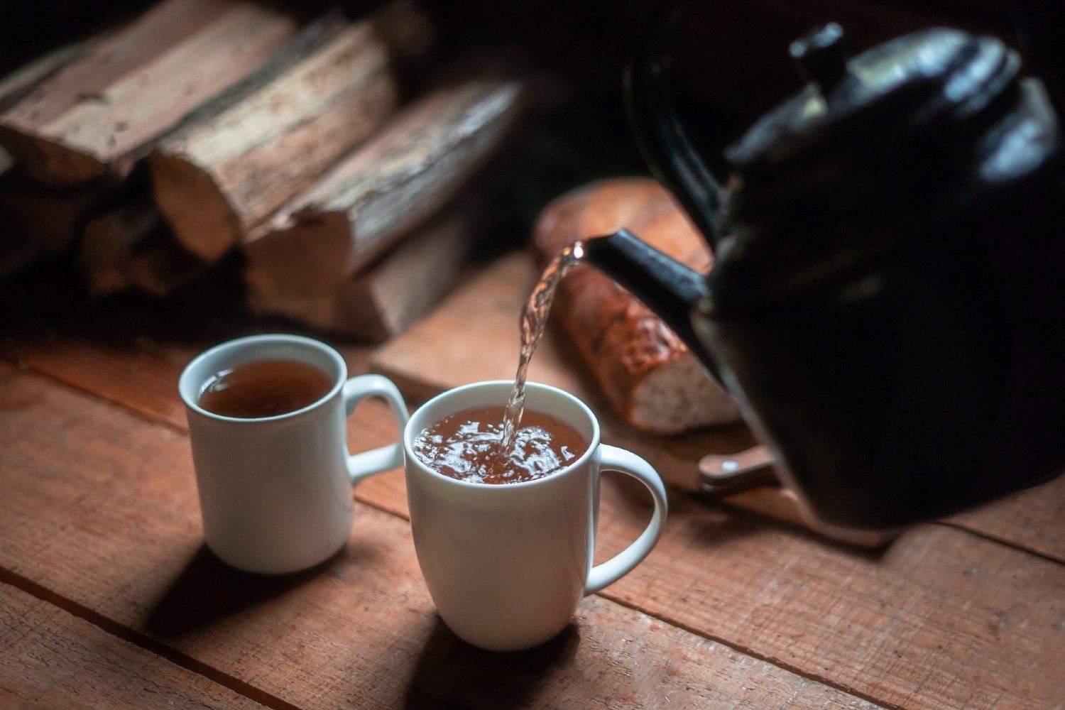 Bedtime tea being poured into white ceramic mugs on a wooden table.