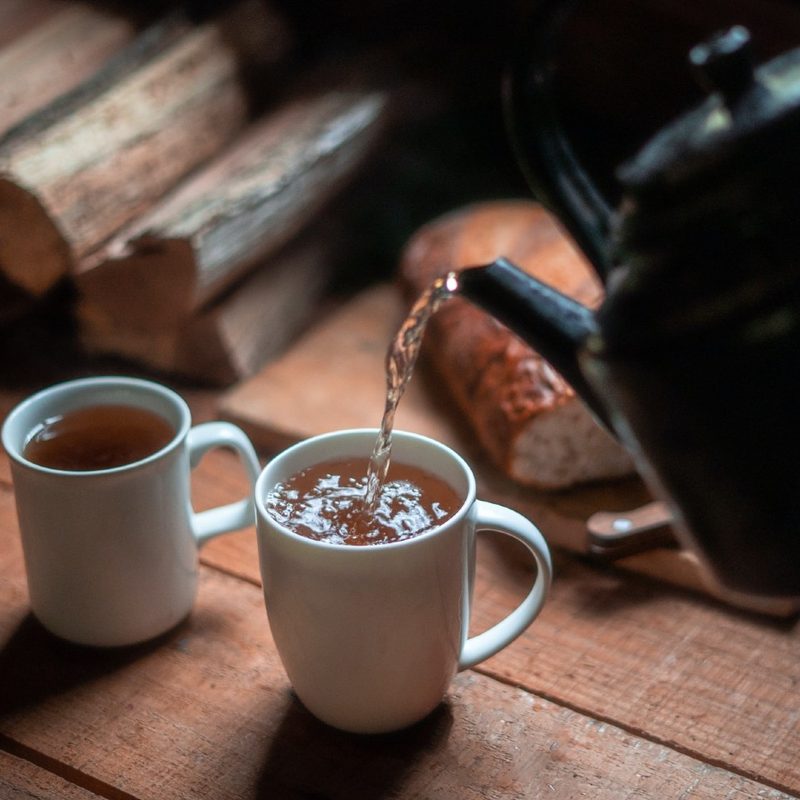 tea being poured into white ceramic mugs on a wooden table.