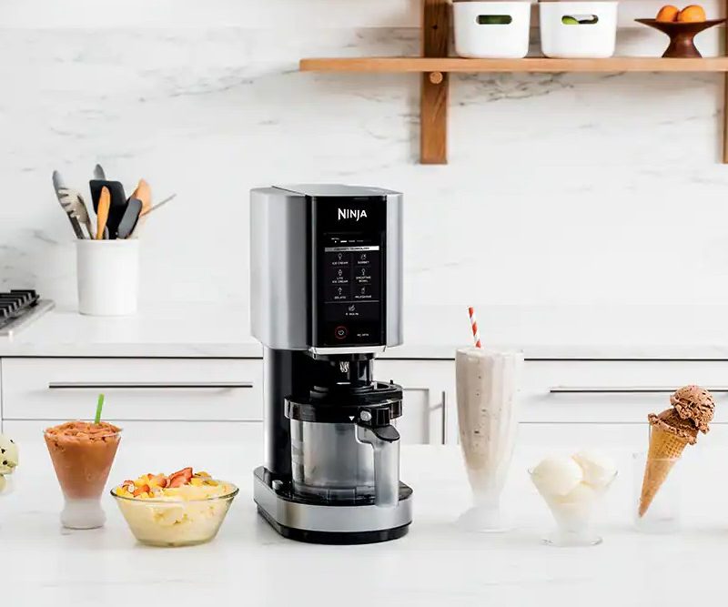 Ninja Creami Ice Cream Maker sitting on a counter with bowls of ice cream.