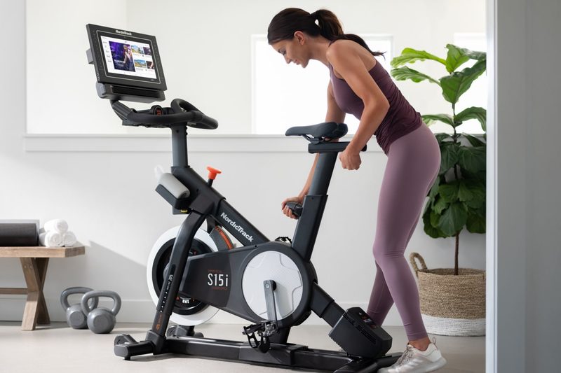 NordicTrack Commercial S15i Studio Cycle being adjusted by a woman in her living room.