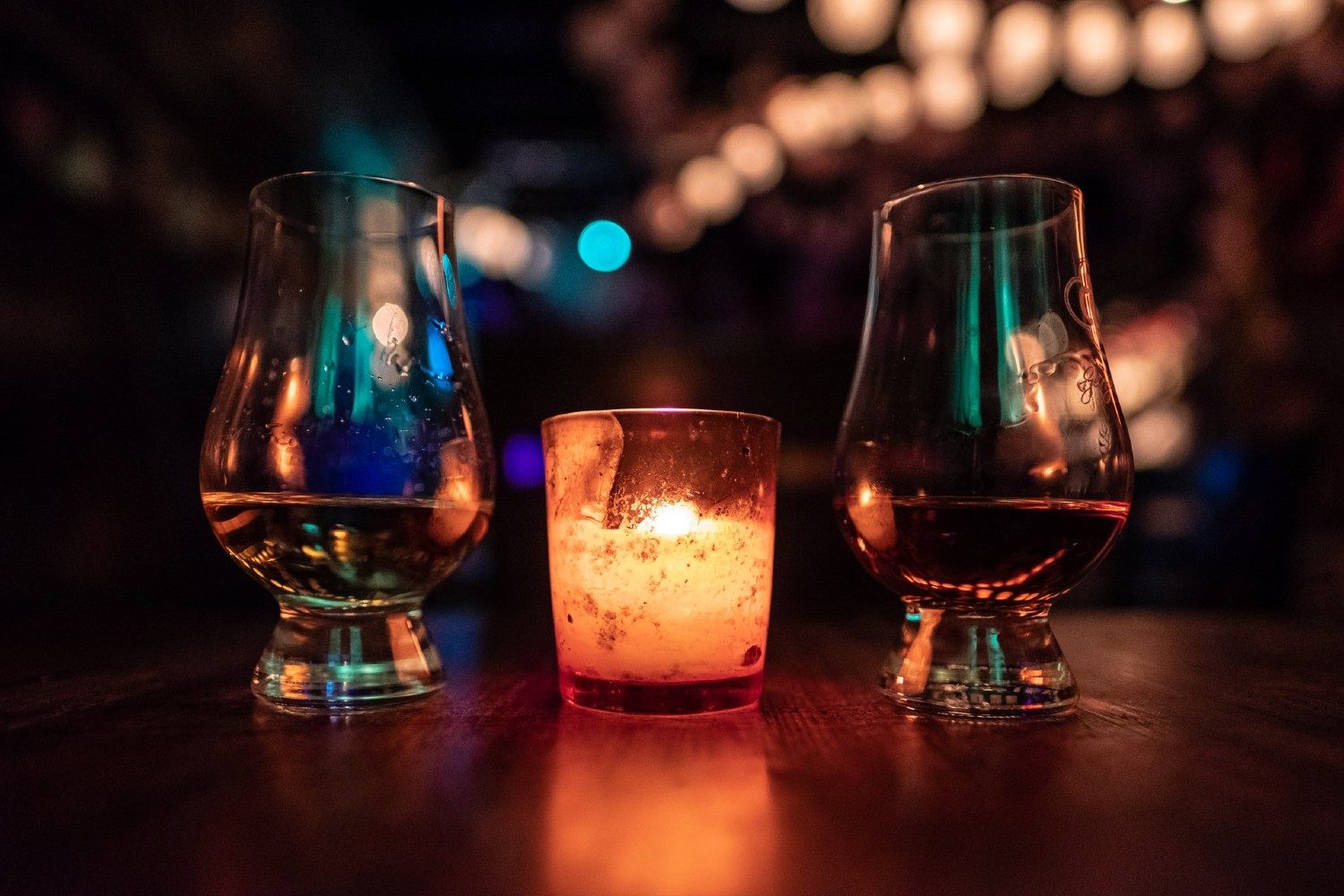 A glass of scotch and a glass of whiskey separated by a lit candle.