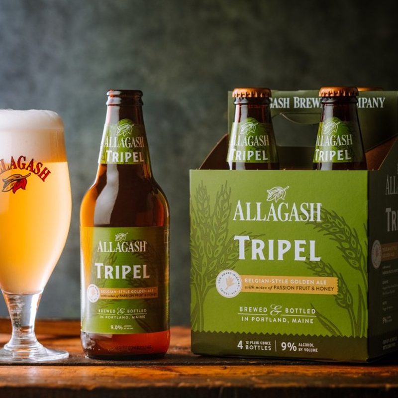 four-pack of Allagash Tripel sitting next to a full glass of beer.