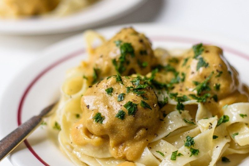 Vegan Swedish meatballs over noodles served on a plate with a knife.