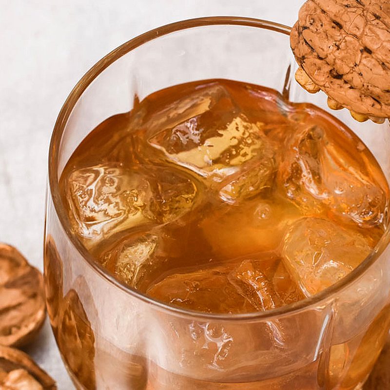 A glass of walnut and maple old fashioned beside walnuts.