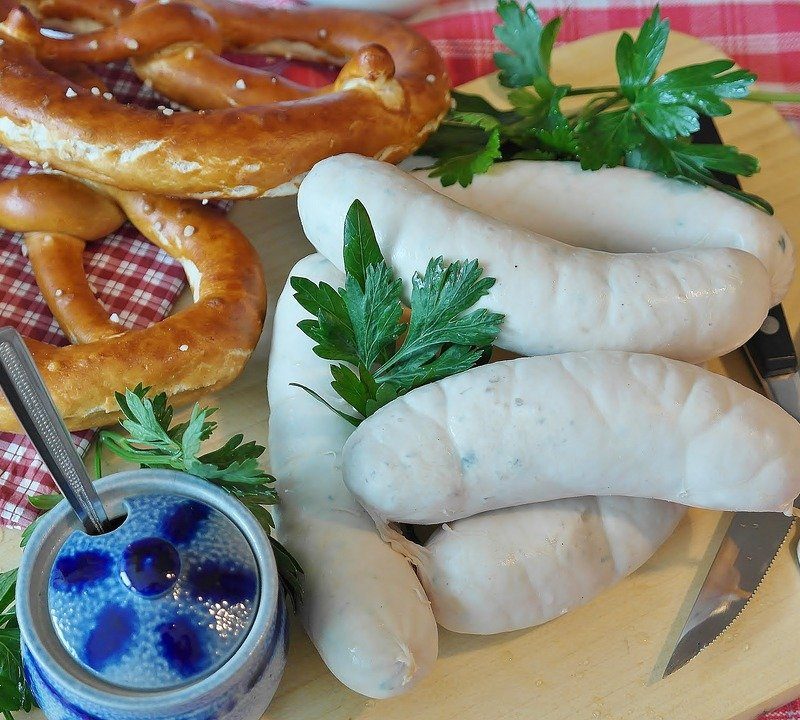 Weisswurst sausage with pretzel on cutting board.