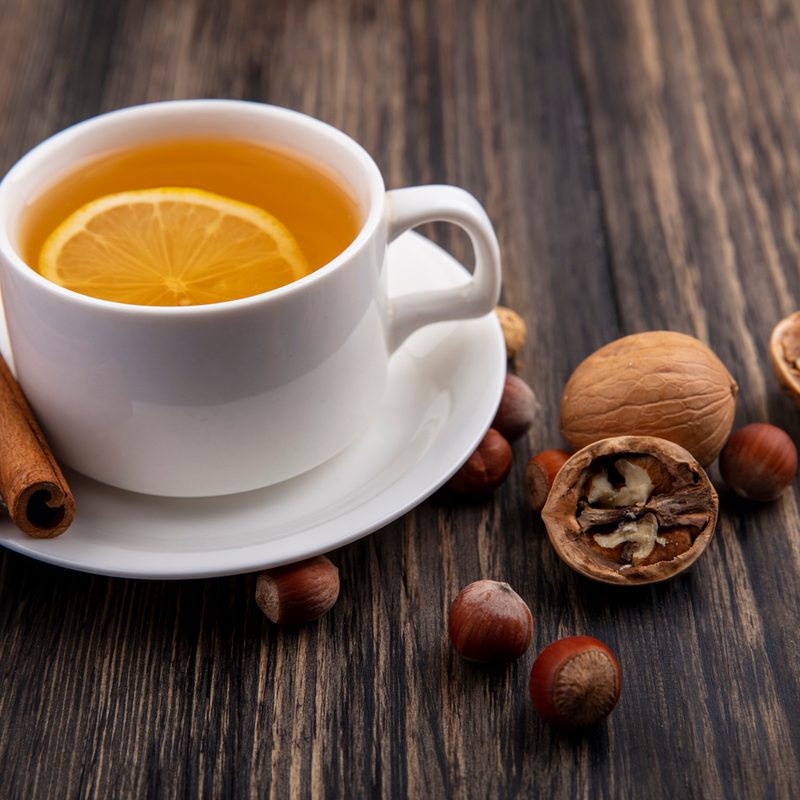 Side view of cup of hot toddy with cinnamon on saucer and nuts walnuts on wooden background