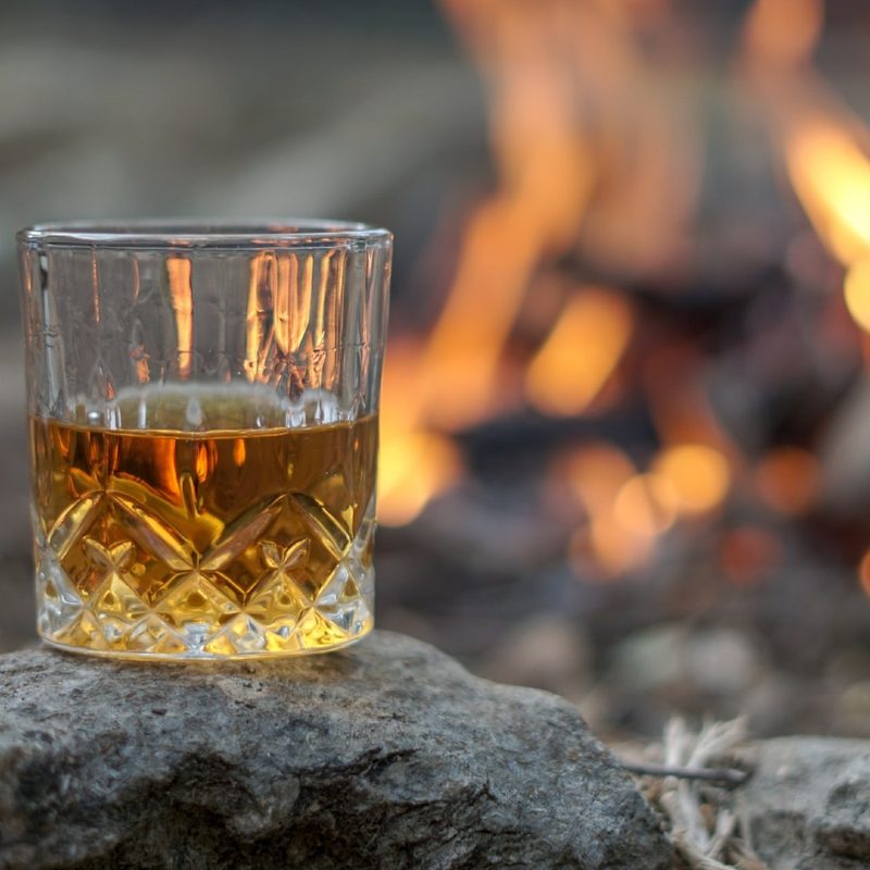 whiskey in a crystal glass sitting on a rock in front of a fire.