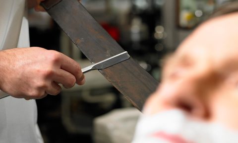 A barber sharpening a straight razor.