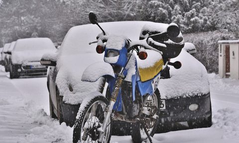 motorcycle standing in front of a car covered in snow.