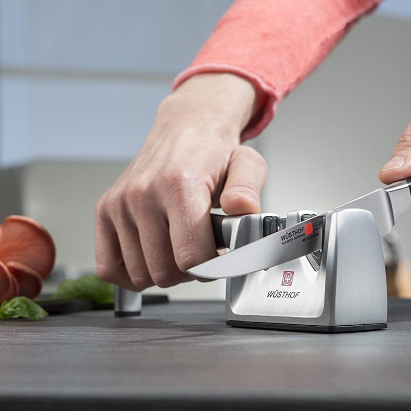 A person placing a Wutshof knife on a Wusthof knife sharpener in the kitchen.