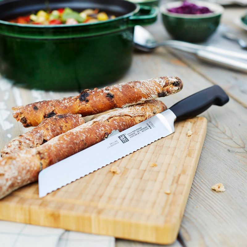 A Zwilling knife beside breadsticks on a wooden cutting board.