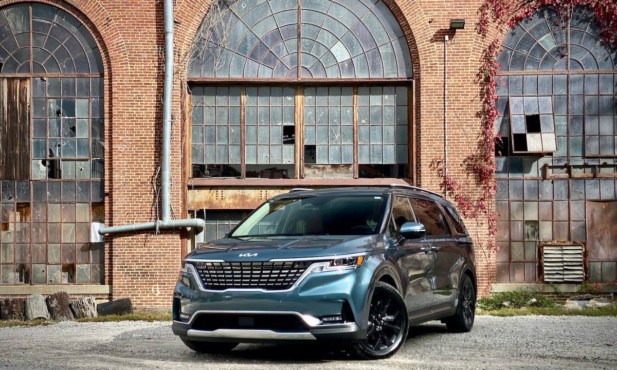 Kia Carnival front end angle from driver side in front of old building.