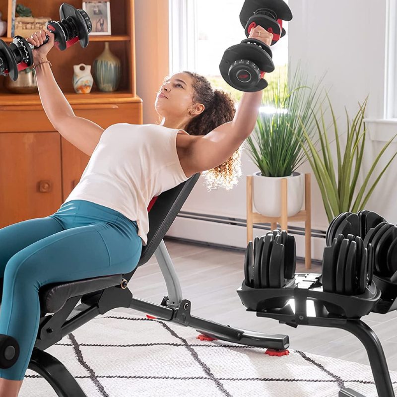 A woman lifting Bowflex SelectTech 552 Adjustable Dumbbells with a Bowflex stand nearby.