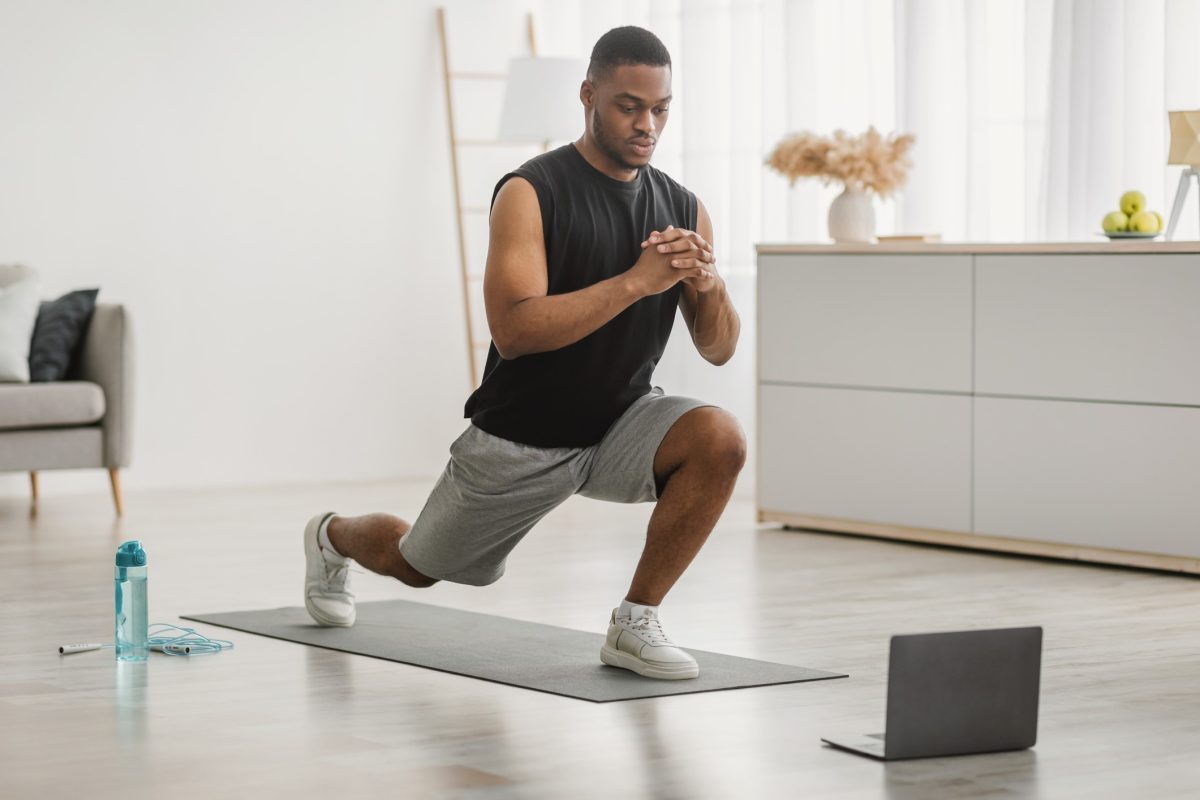 Man doing alternating forward lunges in front of a laptop at home.