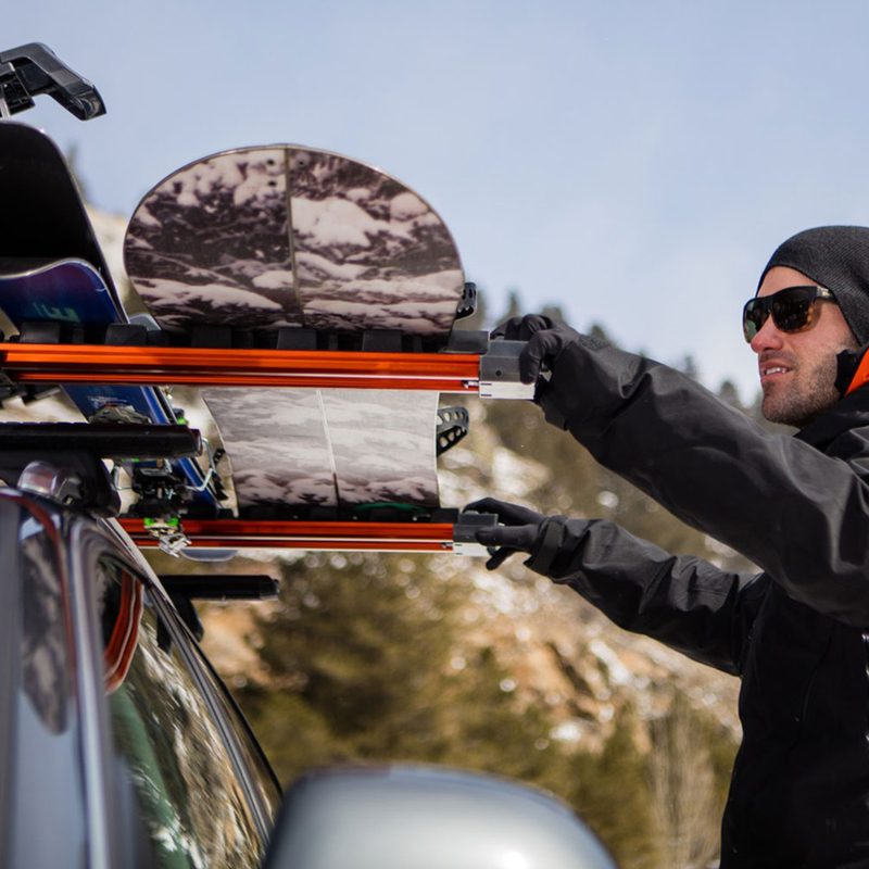 Man packing snowboard gear on a rack on top of his vehicle