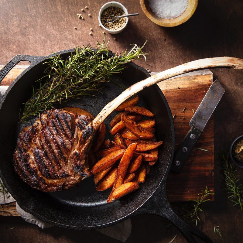 Bone-in, cowboy cut ribeye in a cast iron with fries.