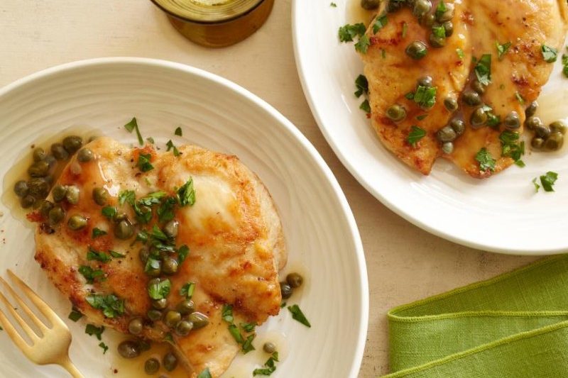 two plates of chicken piccata sitting on a table.