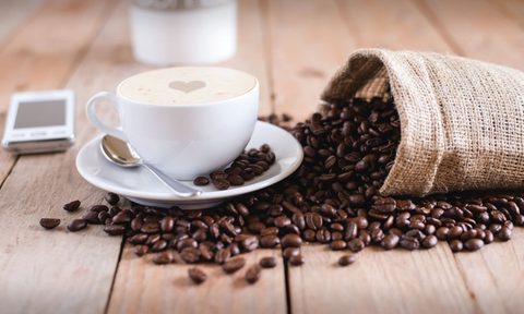 A cup of coffee beside spilled coffee beans