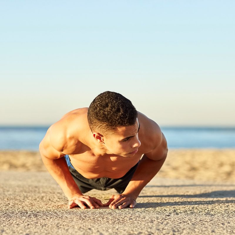 Shirtless athlete doing diamond push-ups at the beach.