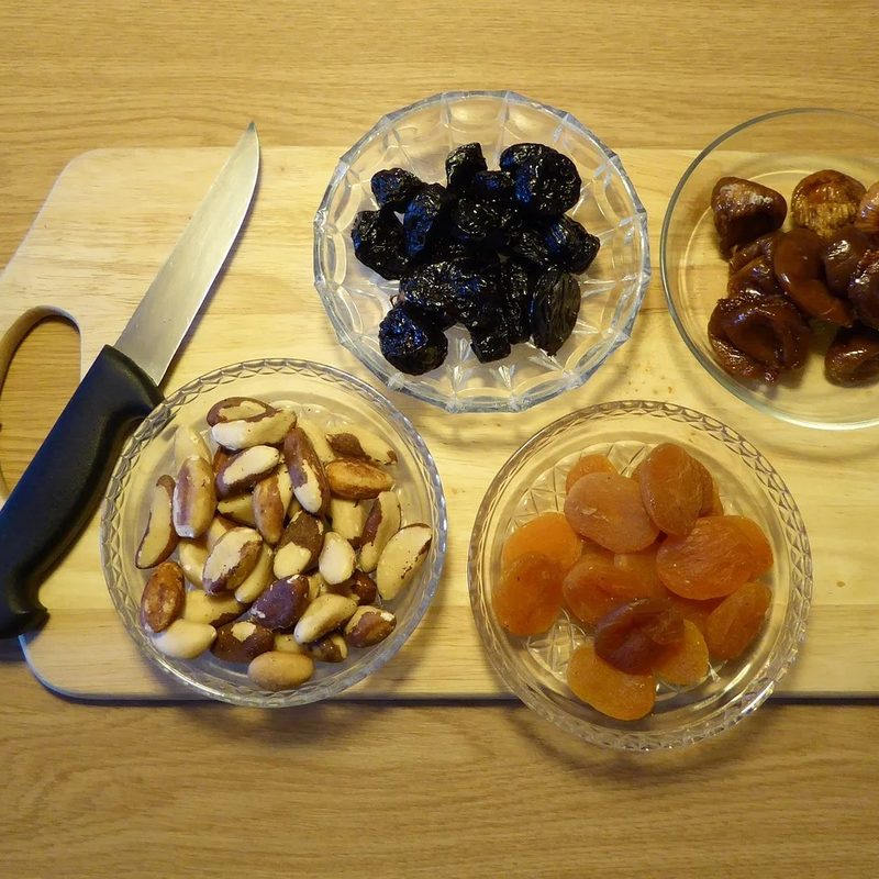 A knife and four bowls of dried fruit on a wooden cutting board.