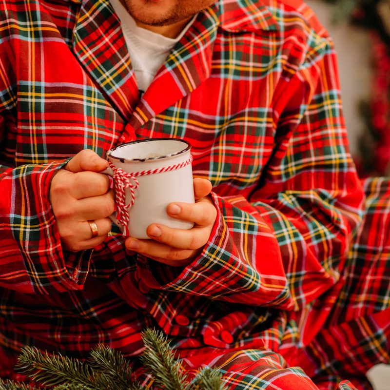 A midsection of a man wearing checkered pajamas and holding a mug at home.