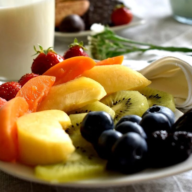 Assorted fruits on a plate with table napkin and a glass of milk in the background