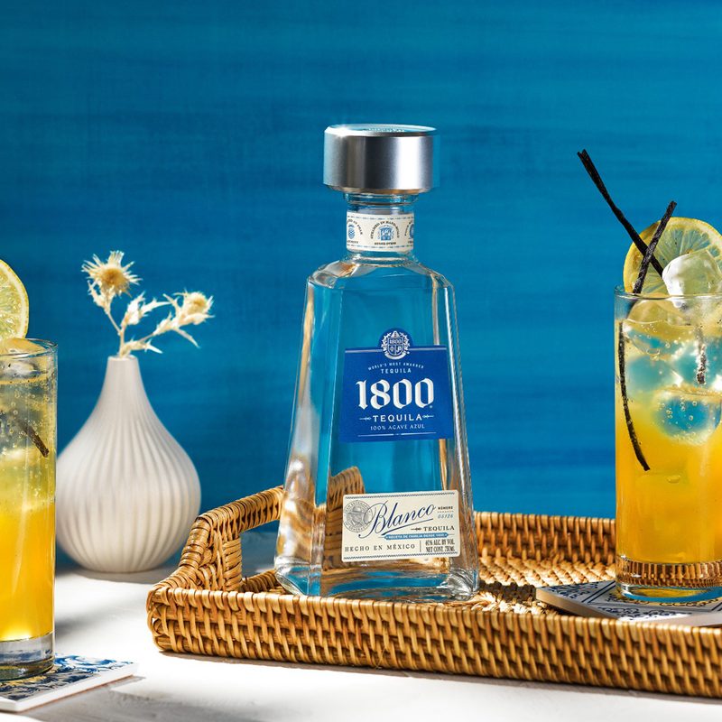 An 1800 Tequila bottle in between two glasses of Fruta de Pasion.