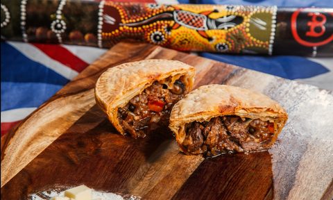 G'day Gourmet meat pie cut in half on cutting board with Australian flag in background.