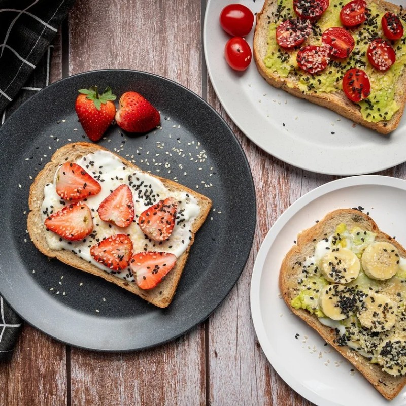 three whole grain pieces of toast on plates with fruits and vegetables.